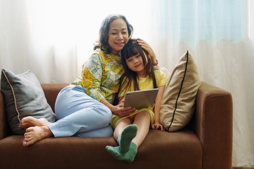 Asian portrait, Grandma and granddaughter doing recreational activities playing tablet computers on the sofa.