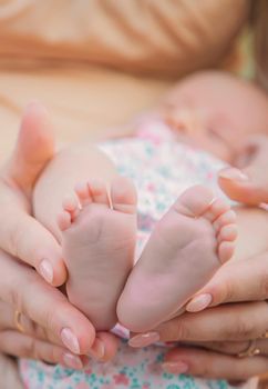 Feet of a newborn baby in mom's hands. Selective focus. People.