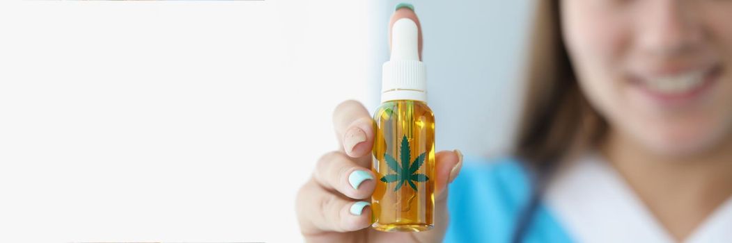 Close-up of medical worker present cannabis oil in plastic bottle for alternative treatment. Cute nurse prescribe hemp to patient. Medicine, health concept