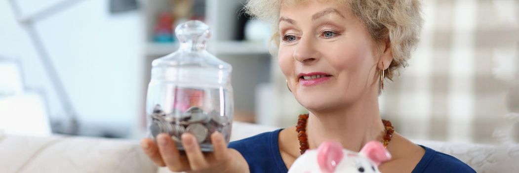 Portrait senior woman hold glass container with saved money for retirement. Put coin in piggybank every day. Financial education, saveup for future concept