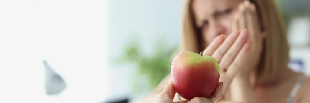 Close-up of blonde woman refuse to eat apple because of teeth pain. Poor female close cheek with hand, dentist needed. Dental problem, healthcare concept