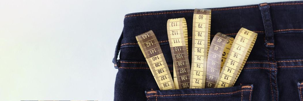 Close-up of yellow measuring tape in jeans pocket image of body slimming. Tool to measure body volume in atelier. Weight loss and weight control concept