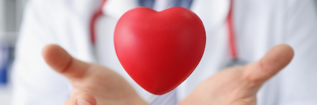 Close-up of medical worker throw red plastic heart and catch it in palms. Save life through donation or charity. Medicine, cardiology, healthcare concept