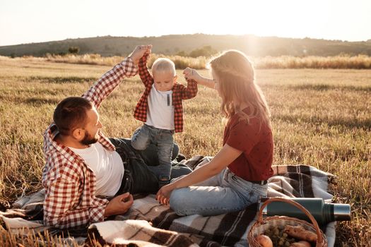 Happy Young Family Mom and Dad with Their Little Son Enjoying Summer Weekend Picnic Outside the City in Field at Sunny Day Sunset, Vacation Time Concept