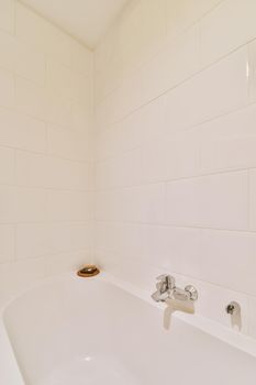 Bathtub with glass shower placed in corner near sink and mirror in small light bathroom with white tile walls