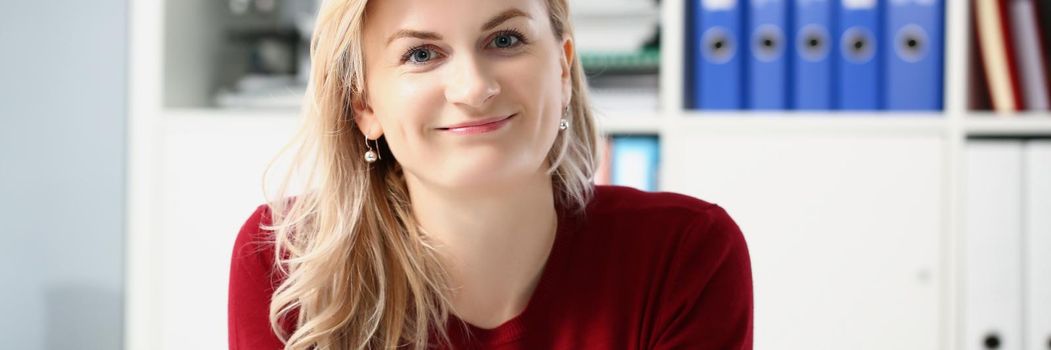 Portrait of beautiful young woman office worker posing in personal cabinet. Smiling female in trendy red pullover. Work, career, business, modeling concept