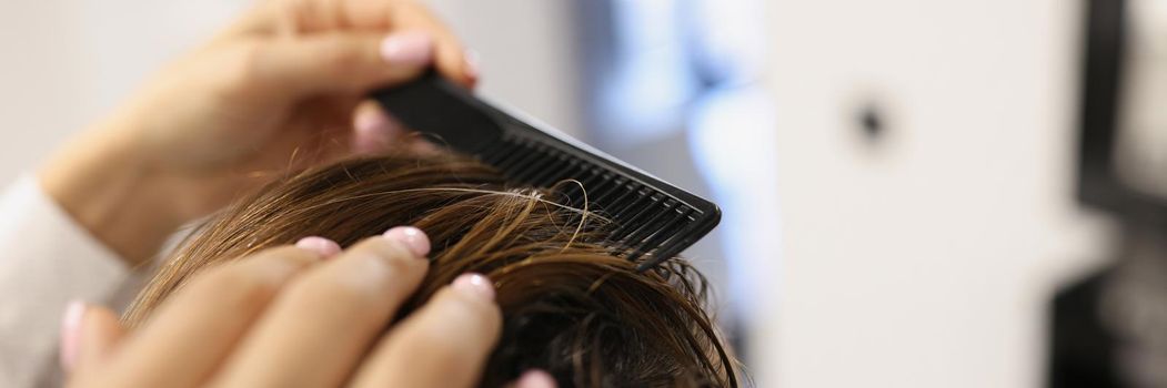 Close-up of professional hairdresser use comb for creating stylish haircut. Client female sitting on appointment in beauty salon. Fashion, barber concept