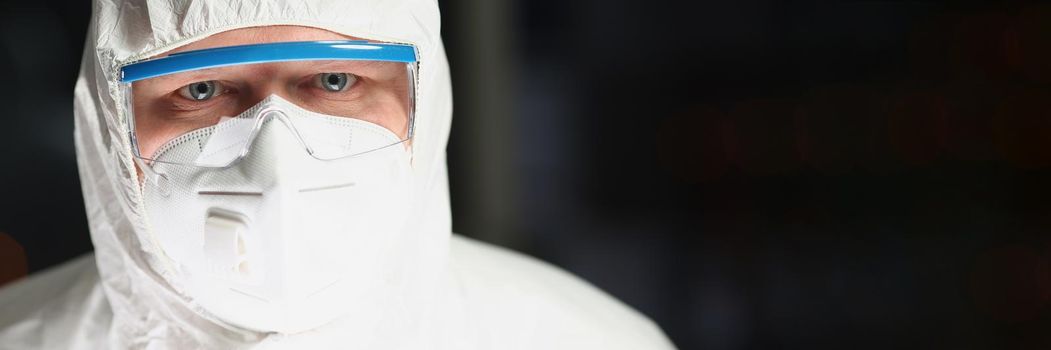 Portrait of worker in protective respirator and white coverall analyzing science experiment. Male chemist in eyeglasses work on research. Science concept