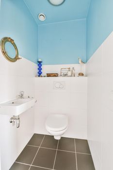 Wall hung toilet and small sink in corner in lavatory room with beige tile