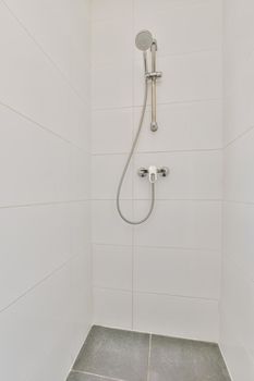 Shower faucets attached to tiled wall near glass partition and ornamental curtail in washroom at home