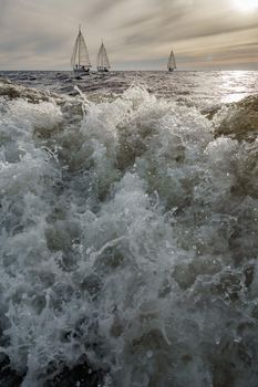 Splashes water of motor boat in the foreground, sailing yachts at sunset in background, sail regatta, big waves. High quality photo