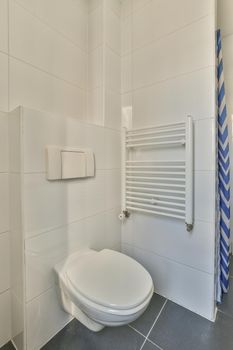 Modern flush toilet and ceramic sink installed on white tiled walls near mirror and towel in small restroom at home