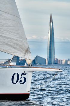 Bowsprit of sailing yacht in sailing regatta at sunset, still water, the clear sky, hot racing, skyscraper on a background. High quality photo