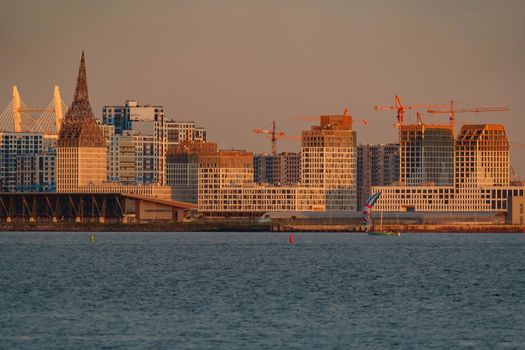 The residential complex under construction on the embankment of the Neva River on Vasilievsky island in sunset, bulk island, construction cranes. High quality photo