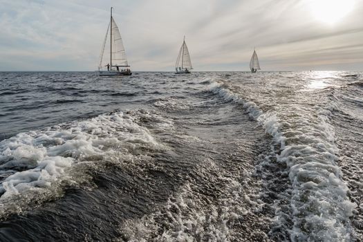 Splashes water of motor boat in the foreground, sailing yachts at sunset in background, sail regatta, big waves. High quality photo