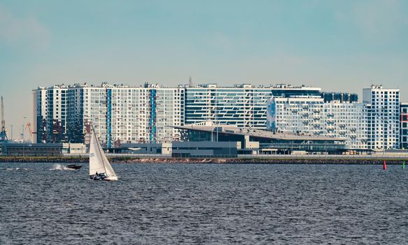 Russia, St. Petersburg, 10 June 2022: The residential complex under construction on the embankment of the Neva River on Vasilievsky island in sunny day, construction cranes, sailing yachts. High quality photo