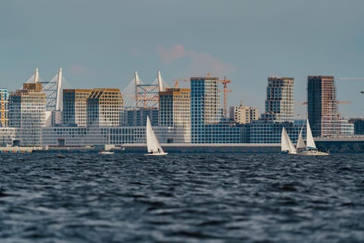 The residential complex under construction on the embankment of the Neva River on Vasilievsky island in sunny day, bulk island, construction cranes, sailing yachts, river navigation. High quality photo