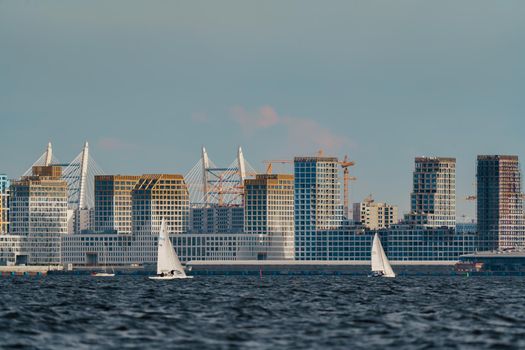 Russia, St. Petersburg, 10 June 2022: The residential complex under construction on the embankment of the Neva River on Vasilievsky island in sunny day, construction cranes, sailing yachts. High quality photo