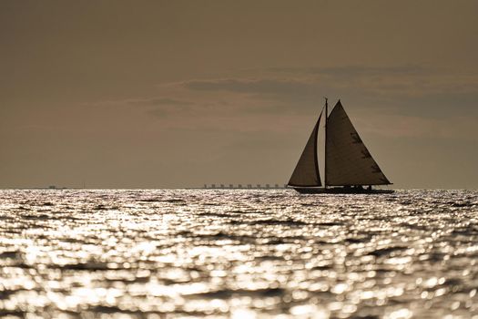 Classic sailing yacht in sea at sunset, the clear sky, sun reflection on water. High quality photo