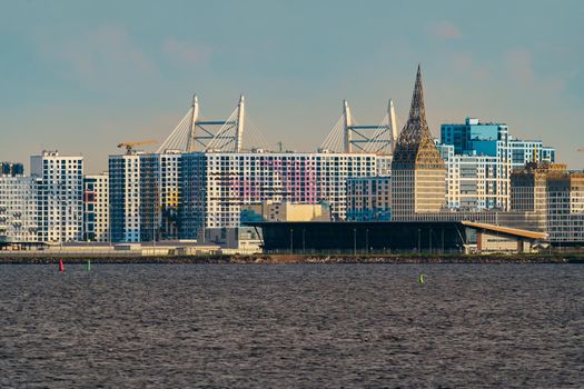 The residential complex under construction on the embankment of the Neva River on Vasilievsky island in sunny day, bulk island, construction cranes, sailing yachts, river navigation. High quality photo