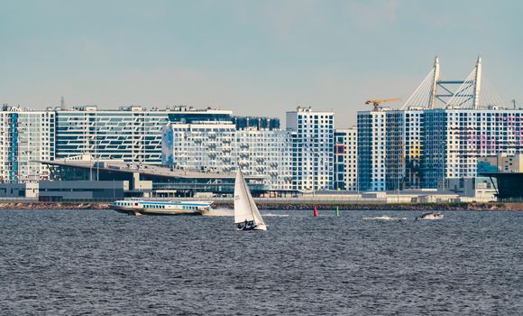 Russia, St. Petersburg, 10 June 2022: The residential complex under construction on the embankment of the Neva River on Vasilievsky island in sunny day, construction cranes, sailing yachts. High quality photo