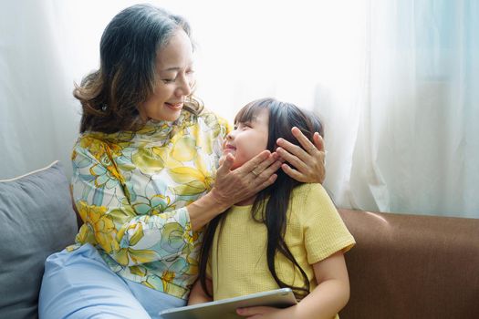 Asian portrait, Grandma and granddaughter doing recreational activities playing tablet computers on the sofa.