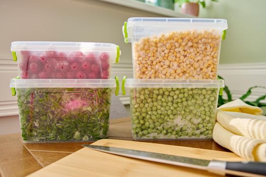 Frozen vegetables and fruits, close-up frozen in the freezer green onions, peas, cherry, corn in plastic containers. Seasonal vegetables, food preparations for the winter