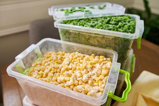 Frozen vegetables and fruits, close-up frozen in the freezer green onions, corn in plastic containers. Seasonal vegetables, food preparations for the winter