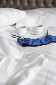 two cups of coffee and a beautiful bra on a white bed, close-up