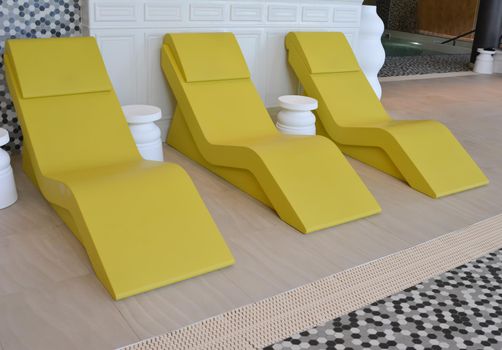 line of three yellow chaise longue in the pool