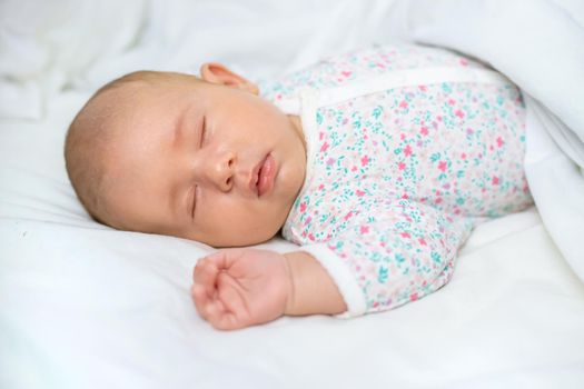 Newborn baby sleeps on a white bed. Selective focus. People.