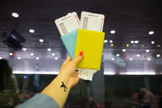 The girl holds two passports in her hands while standing in the airport.