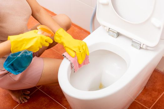 Woman cleaning toilet seat using liquid spray and pink cloth wipe restroom at house, female wearing yellow rubber gloves she sitting and wash cleaner bowl bathroom wc, Housekeeper healthcare concept