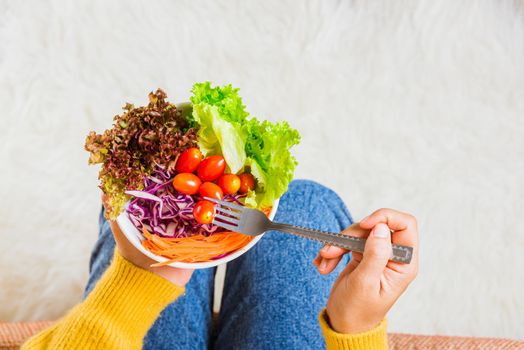 Young woman eating fresh salad meal vegetarian spinach in a bowl, top view of female hands holding bowl with green lettuce salad on legs, Clean detox healthy food concept