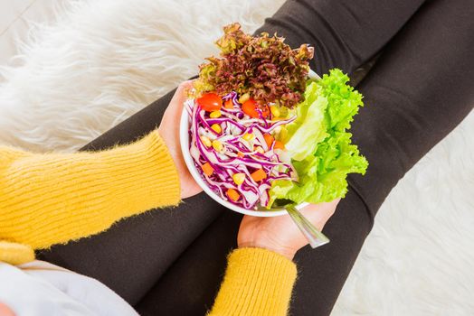 Female hands holding bowl with green lettuce salad on legs, Above young woman eating fresh salad meal vegetarian spinach in a bowl, Clean detox healthy homemade food concept
