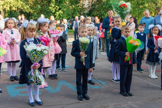 NOVOKUZNETSK, KEMEROVO REGION, RUSSIA - SEP, 1, 2021: Meeting with the first-grade pupils and teacher at schoolyard. The day of knowledge in Russia.