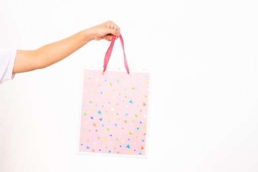 Closeup women hand holding a colorful pink shopping bag, studio shot isolated on white background, female holds in hand white clear empty blank craft paper gift bag for purchases