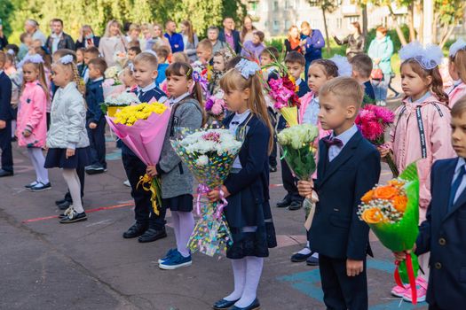 NOVOKUZNETSK, KEMEROVO REGION, RUSSIA - SEP, 1, 2021: Meeting with the first-grade pupils and teacher at schoolyard. The day of knowledge in Russia.