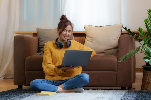 Portrait of Happy young asian woman is relaxing on comfortable couch and using laptop at home. Relax concept