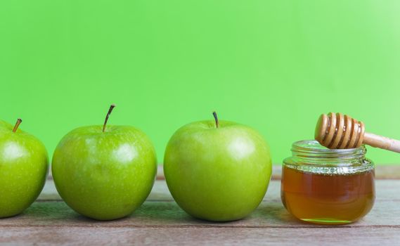 Jewish holiday, Apple Rosh Hashanah, on the photo have honey in jar and green apples on wooden with green background
