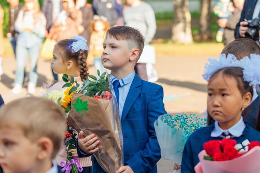 NOVOKUZNETSK, KEMEROVO REGION, RUSSIA - SEP, 1, 2021: Meeting with the first-grade pupils and teacher at schoolyard. The day of knowledge in Russia.