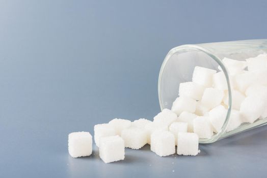 White sugar cube sweet food ingredient spilled out of the glass, studio shot isolated on a gray background, Minimal health high blood risk of diabetes and calorie intake concept