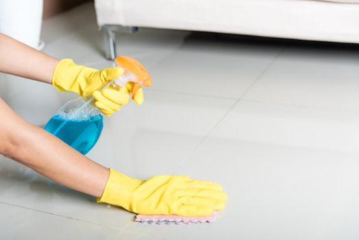 Asian woman wearing yellow rubber glover with cloth rag and detergent spray cleaning floor at home in living room, Female hands wash cleaner, housework and housekeeping concept