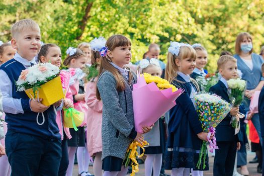 NOVOKUZNETSK, KEMEROVO REGION, RUSSIA - SEP, 1, 2021: Meeting with the first-grade pupils and teacher at schoolyard. The day of knowledge in Russia.