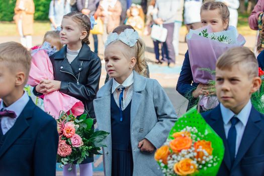 NOVOKUZNETSK, KEMEROVO REGION, RUSSIA - SEP, 1, 2021: Meeting with the first-grade pupils and teacher at schoolyard. The day of knowledge in Russia.