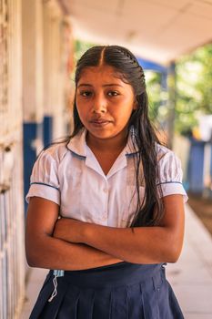 Vertical photo of a Nicaraguan elementary student girl smiling and looking at the camera with her arms crossed in a school in the rural area of Masaya