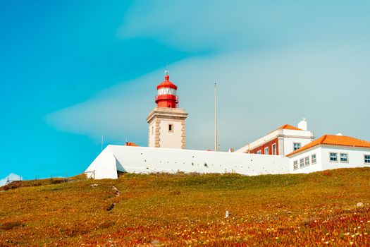 View of the Cabo da Roca Lighthouse. Sintra, Portugal. Portuguese Farol de Cabo da Roca is a cape which forms the westernmost point Eurasian land mass. Sunny summer day. Cloudy sky