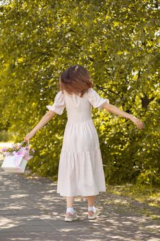 A beautiful bouquet of flowers in a box in the hands of a beautiful girl who walks along the street on a sunny day. Girl in a dress, glasses and sneakers. Focus on the background of flowers.