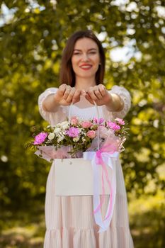 A beautiful bouquet of flowers in a box in the hands of a beautiful girl who walks along the street on a sunny day. Girl in a dress, glasses and sneakers. Focus on the background of flowers.