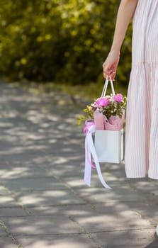 A beautiful bouquet of flowers in a box in the hands of a beautiful girl who walks along the street on a sunny day. Girl in a dress, glasses and sneakers. Focus on the background of flowers.